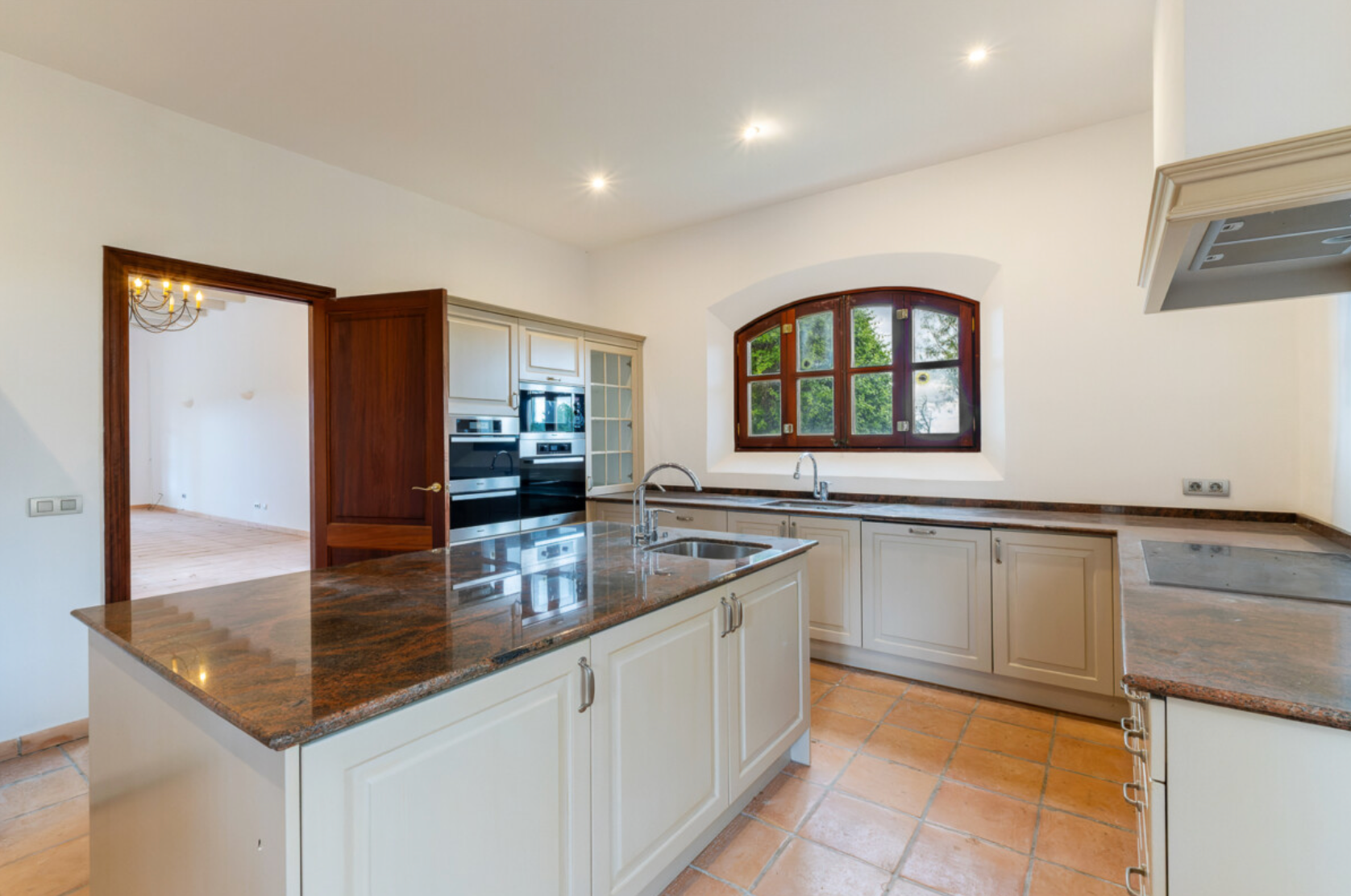 Modern open concept kitchen and living space with white cabinets, wood floors and recessed lighting in luxury apartment.