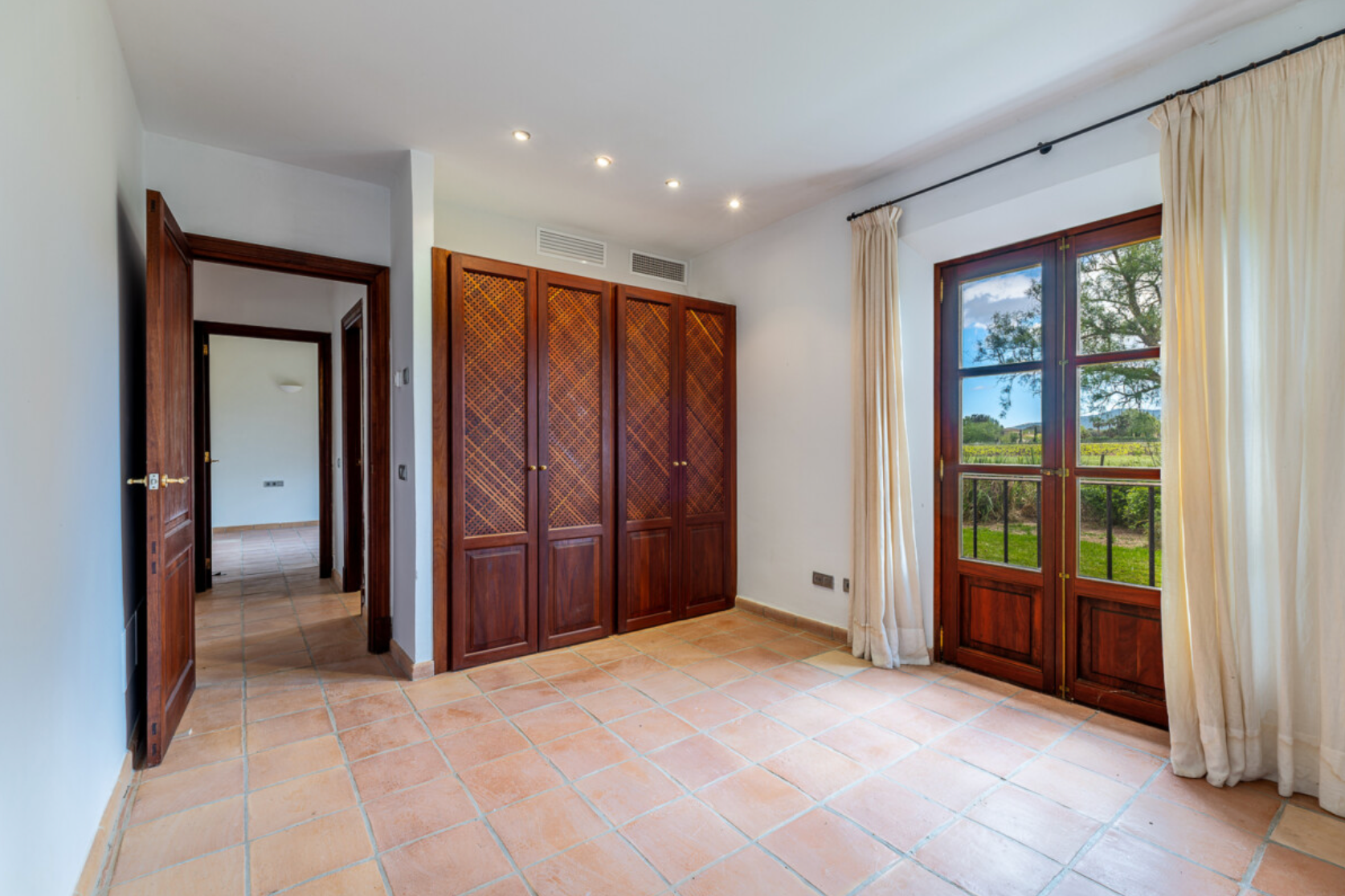 Luxurious modern hallway with recessed lighting, wooden built-in wardrobes, and cream-colored curtains.