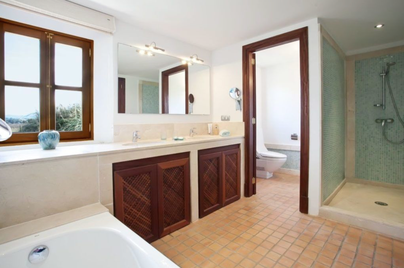 Luxurious bathroom with wooden vanity cabinets, large mirror, and separate shower enclosure featuring beige tile flooring.