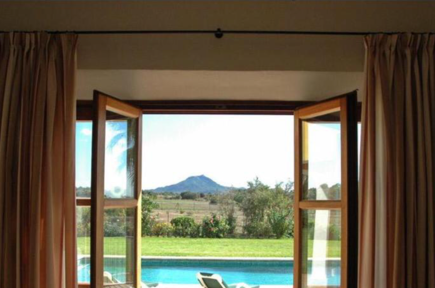 Panoramic mountain views through large windows in a modern living room with brown curtains and comfortable seating.