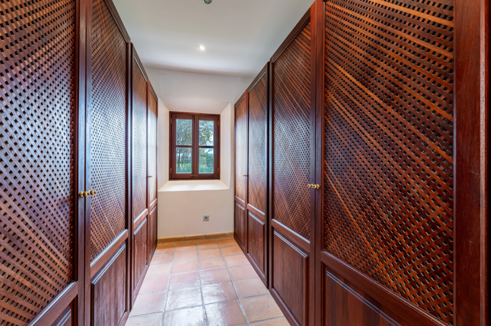 Hallway with rich mahogany wood paneling and lattice details leading to a bright window at the end.