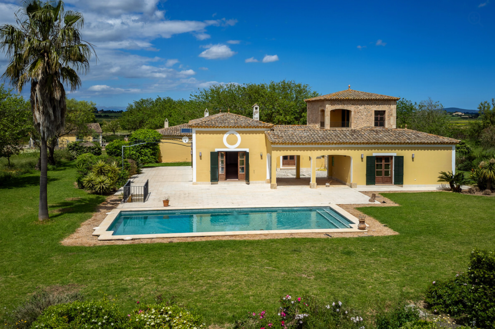 Aerial view of luxury yellow Mediterranean villa with swimming pool and palm tree in landscaped garden on sunny day.