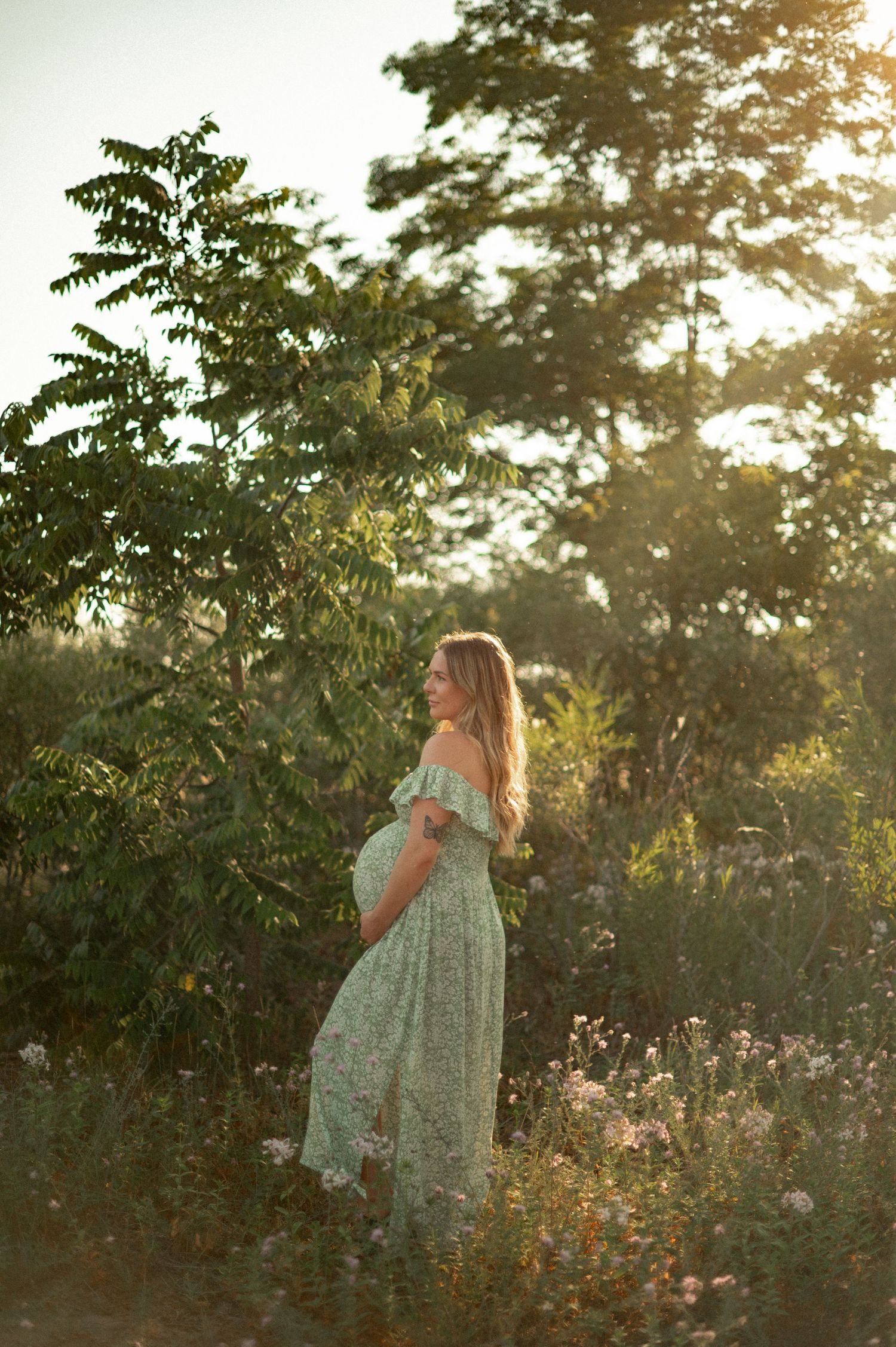 A pregnant woman in jeans and white top sits relaxed on the floor in a bright minimalist setting.