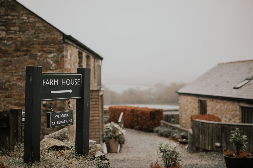 Rustic Farm House wedding venue sign with stone buildings and gravel path on a misty day.