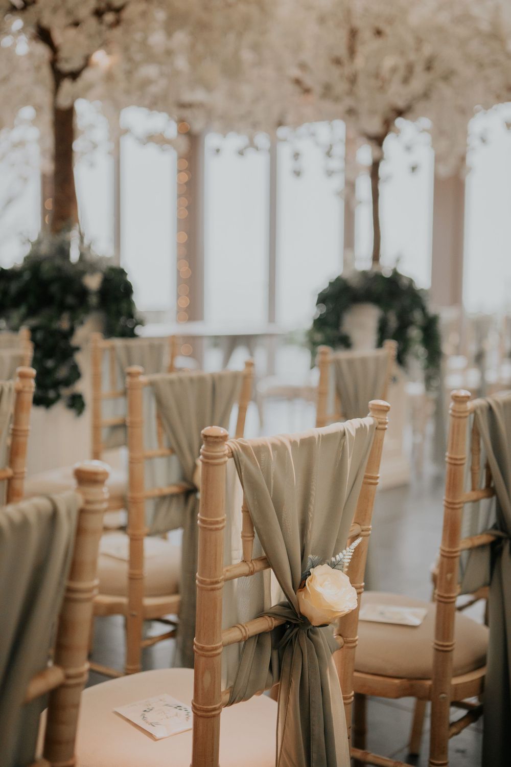 Wooden chiavari chairs with sage green fabric sashes and white rose detail in wedding ceremony.