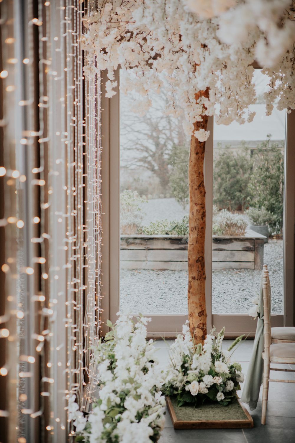 White blossom tree ceremony decor with hanging crystal strands and white floral arrangements.