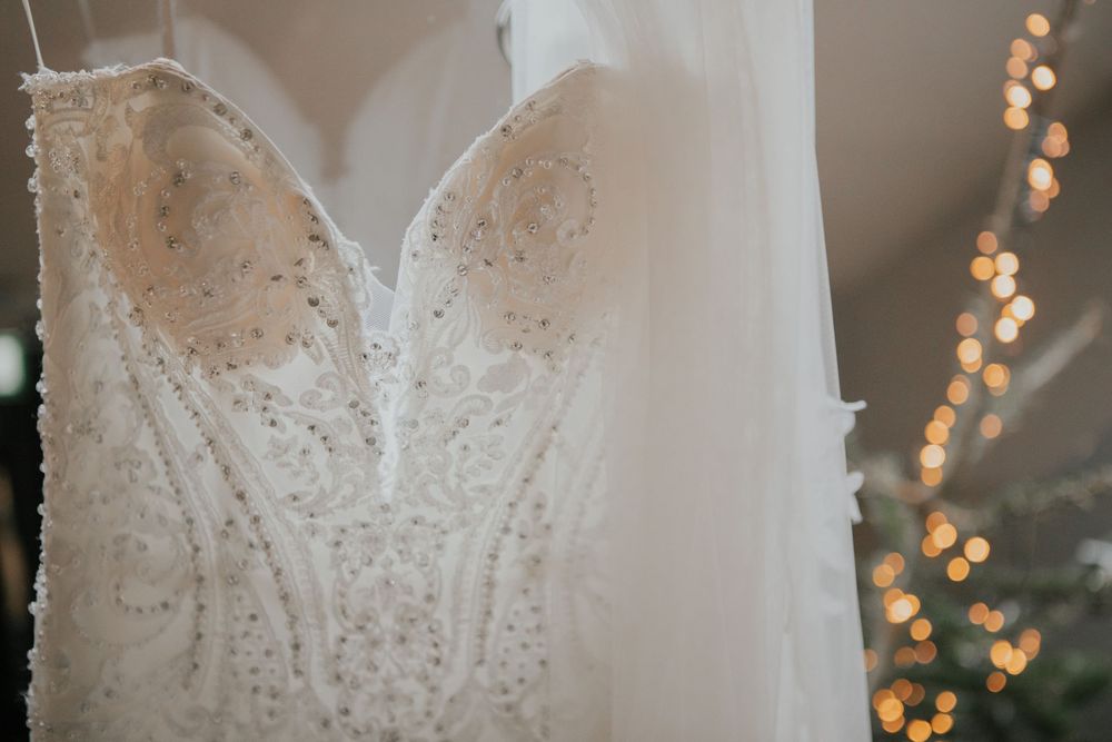 Beaded strapless wedding gown with embellished bodice hanging near warm fairy lights backdrop.