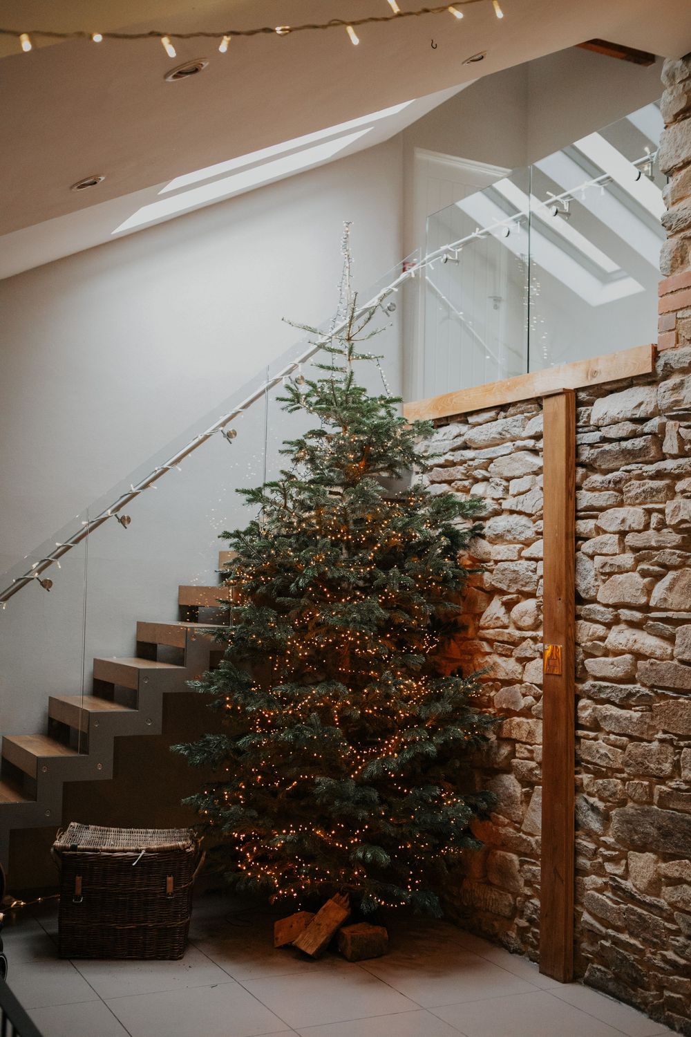 Christmas tree with warm fairy lights beside stone wall staircase in rustic wedding venue.