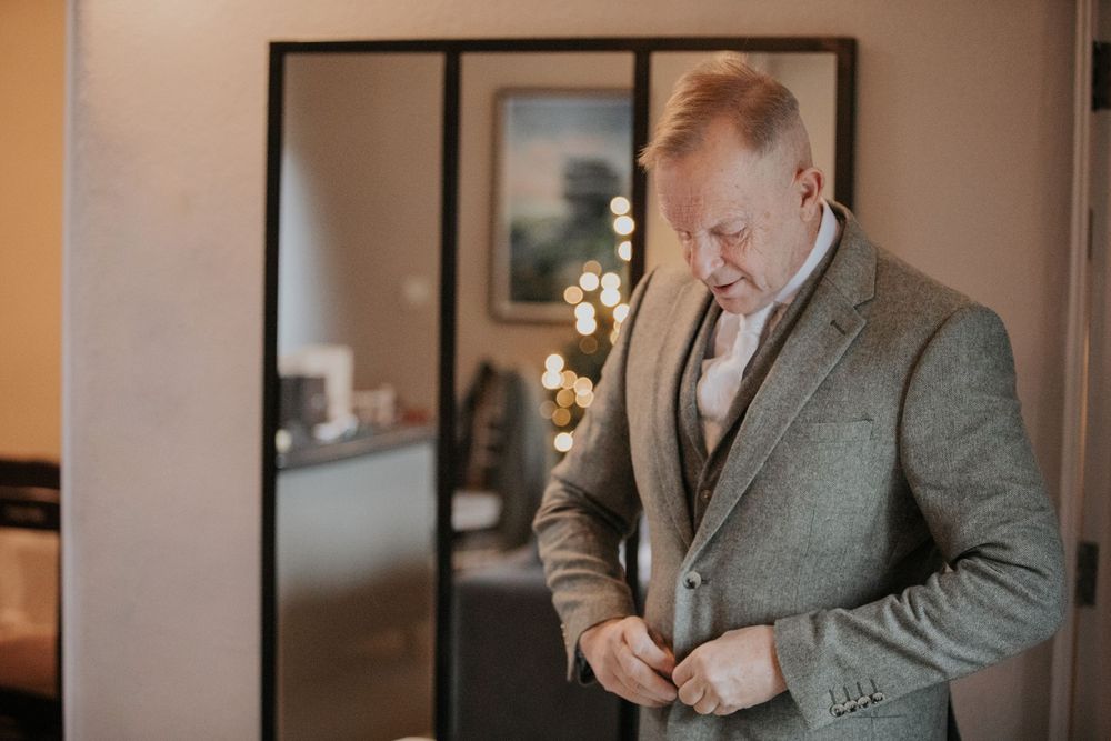 Groom in grey tweed suit adjusting cufflinks while preparing for wedding ceremony.