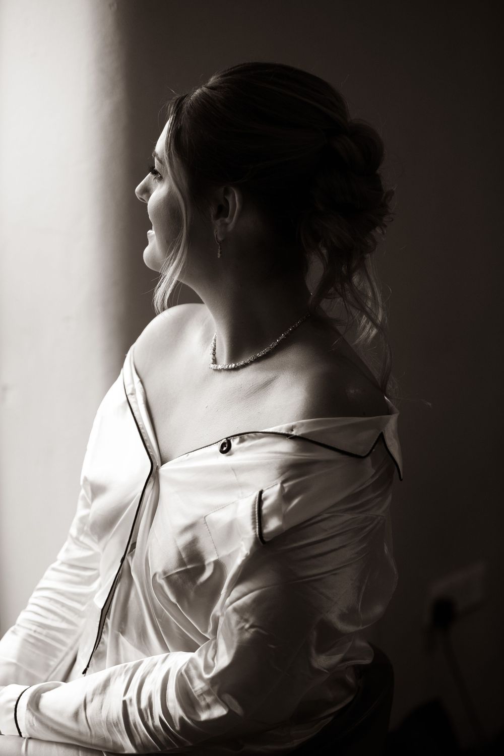Black and white portrait of smiling bride in silk robe by window light.