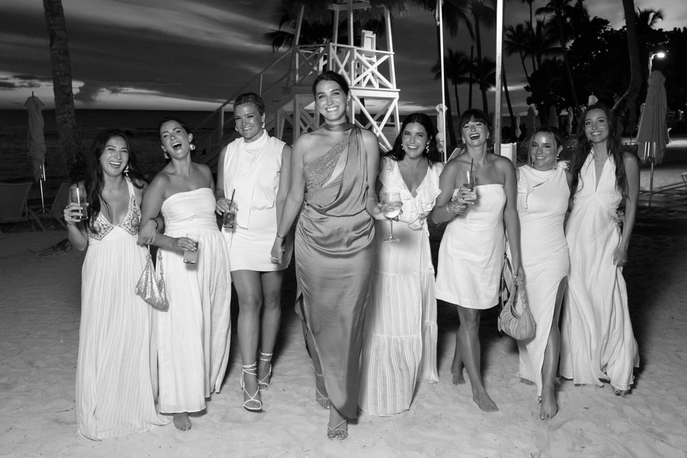 A group of people in elegant white and gray attire pose together at a nighttime outdoor event.