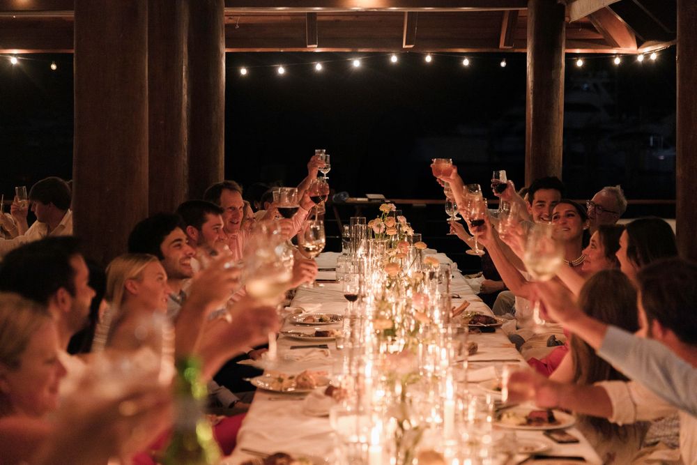 Wedding reception guests raise their arms in celebration during a candlelit evening dinner party.