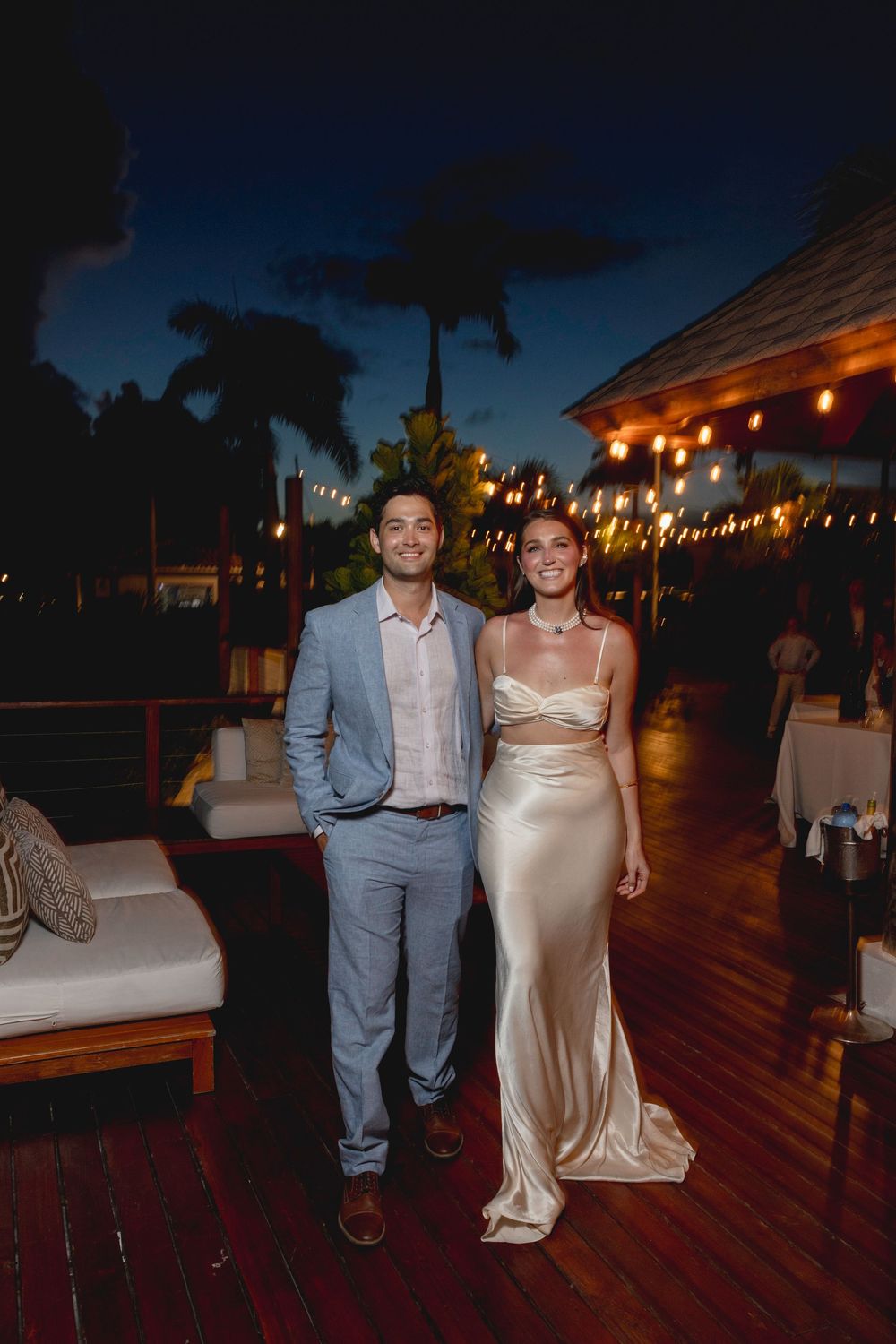 Couple dancing together at an outdoor evening reception with string lights overhead creating a romantic ambiance.