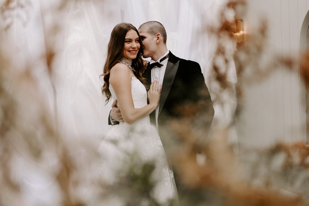 A romantic wedding couple embraces in a dreamy outdoor setting with soft bokeh lighting and autumn foliage.