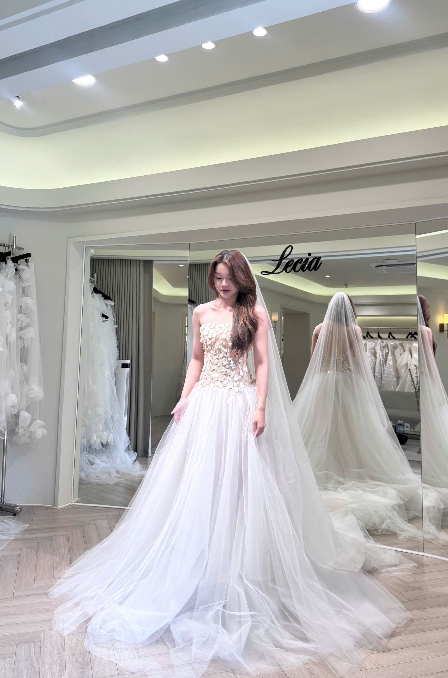 Bride trying on elegant floral embroidered tulle wedding gown in a bridal boutique showroom.