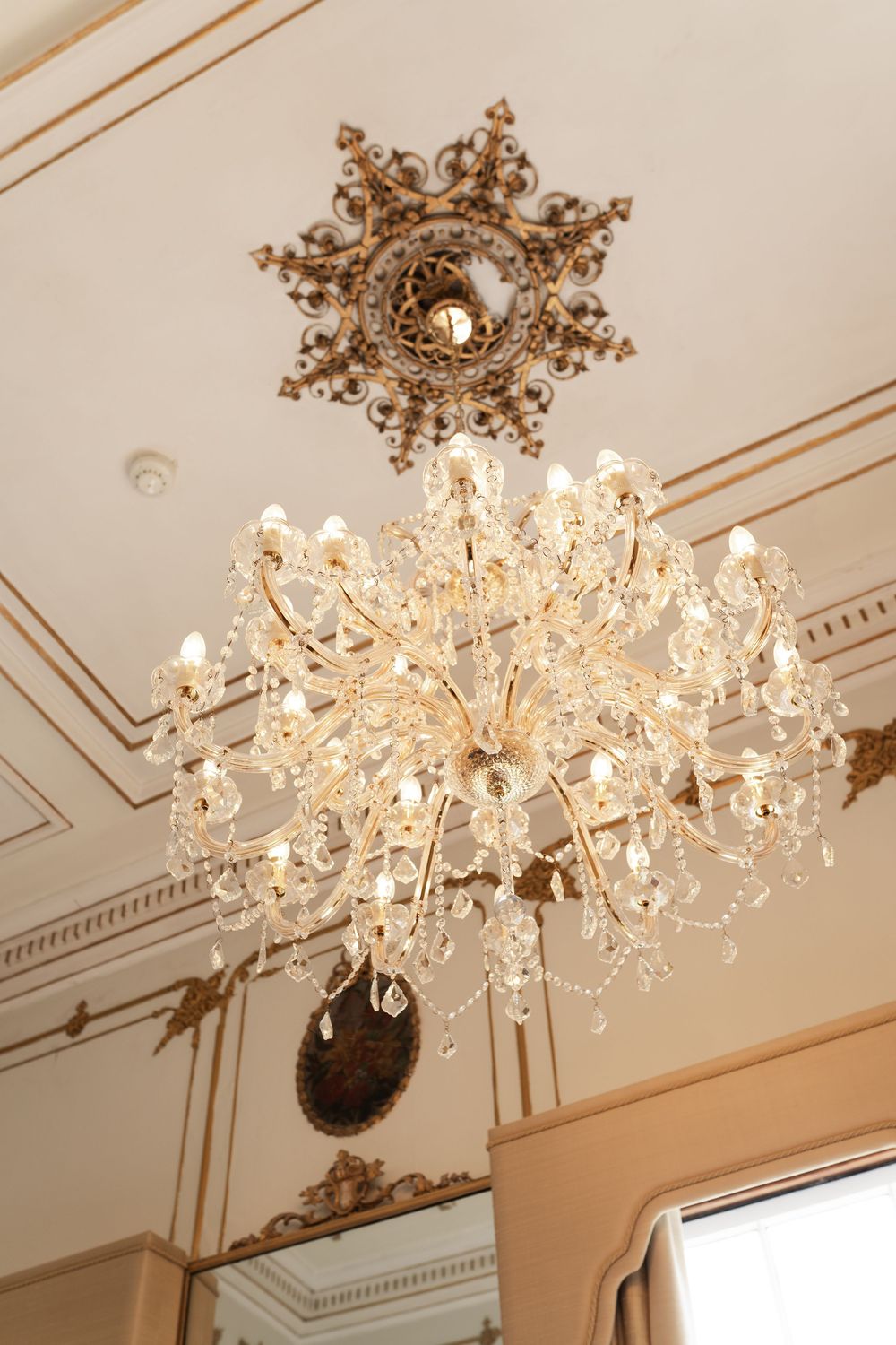 Elegant crystal chandelier with ornate gold accents mounted on a white ceiling with decorative molding details.