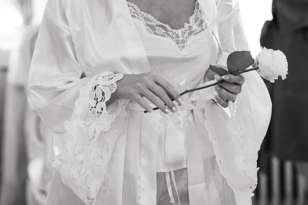 A bride in a white lace wedding dress holds a bouquet while getting ready for her ceremony.