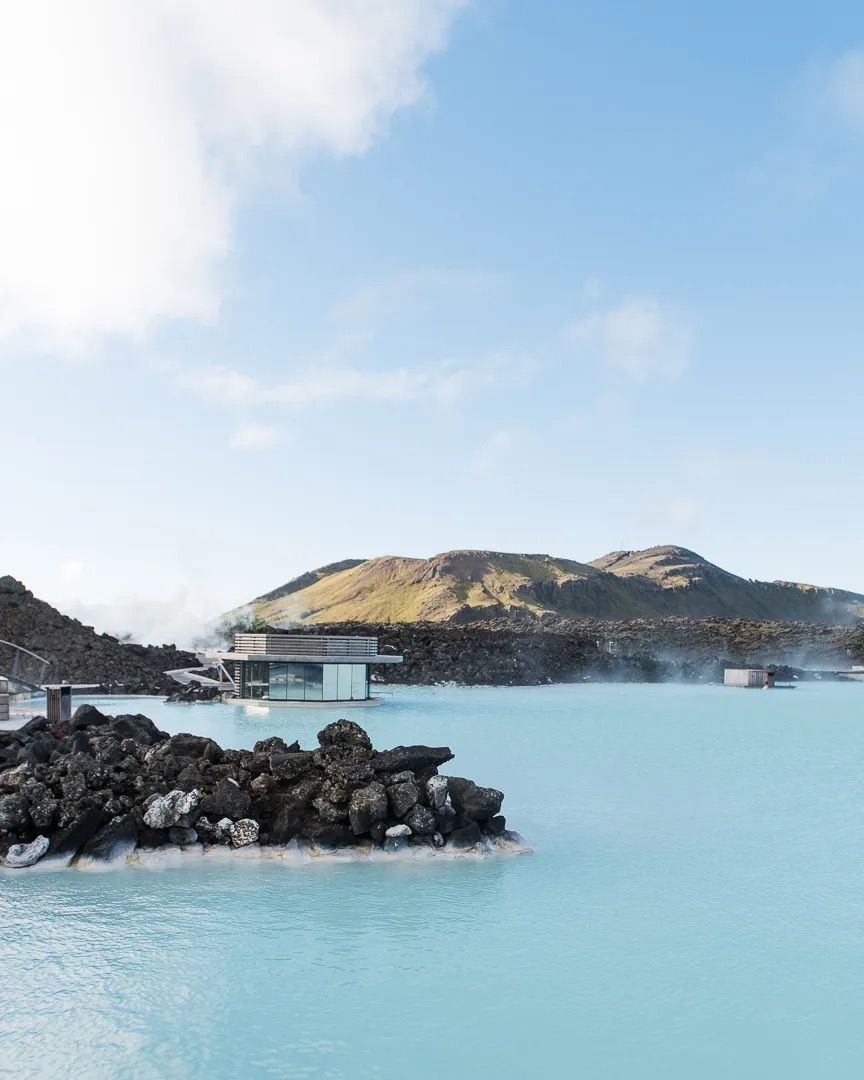 Turquoise geothermal lagoon surrounded by dark volcanic rocks and hills.
