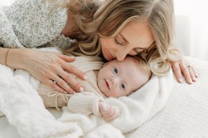 Portrait d’une nouvelle maman qui se penche avec amour sur son bébé couché sur un lit