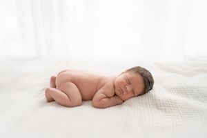 Bébé endormi sur le ventre sur un lit blanc et crème dans une douce lumière au studio
