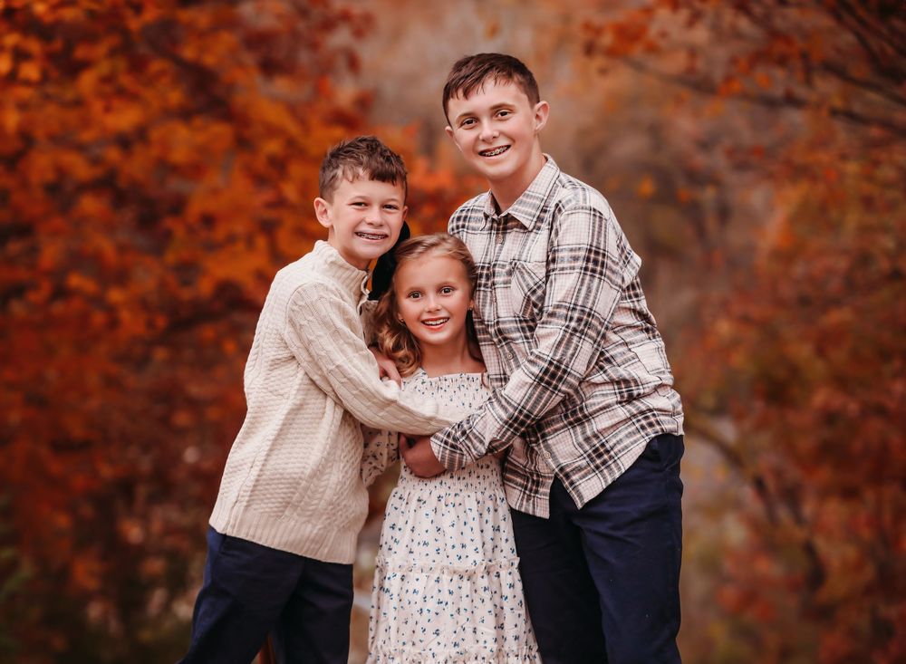 Siblings pose together in autumn forest with vibrant orange foliage and warm lighting. Best child photographer.