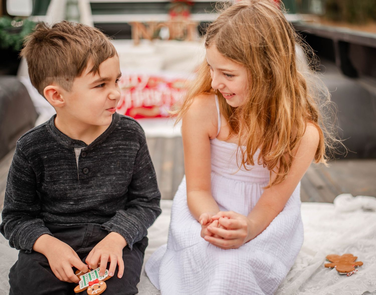Two young children share a sweet candid moment together while sitting outdoors in casual attire.