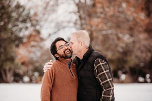 A couple shares tender moments together in a fall setting with brown autumn leaves in the background.