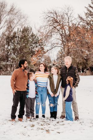 A group sits together in the snow during a winter photo session with bare trees in the background.