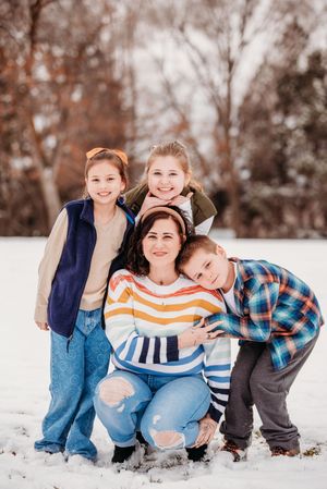 A family in casual winter clothing poses playfully together in the snow during a winter photo session.