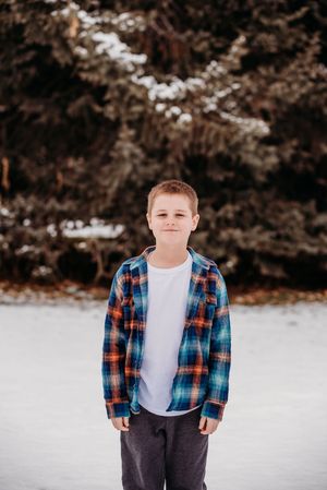 A person in a plaid flannel shirt and white t-shirt poses against a snowy winter backdrop.