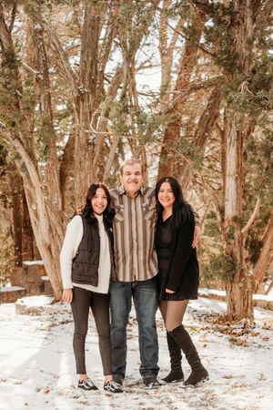 Three people share a laugh together while standing in a snowy wooded area on a winter day.