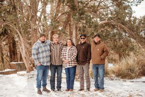 A group of five people standing together outdoors in winter with snow on the ground and trees in the background.