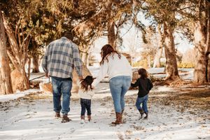 A family walks together hand in hand down a snowy path surrounded by trees on a winter afternoon.
