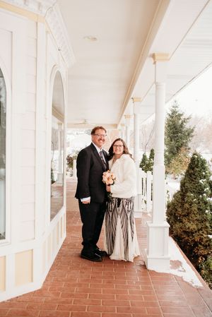 A couple shares a romantic moment on a covered terrace with white columns and terracotta flooring.