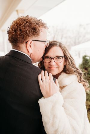 A romantic winter wedding moment captured with the couple embracing while wearing glasses and formal attire.