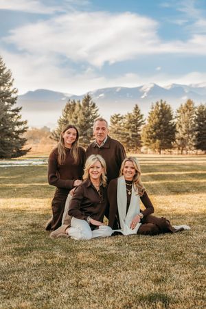 A family of four relaxes together on grassy field with mountains and evergreen trees in background during golden hour.