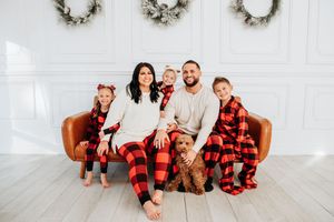 A family wearing matching red and black buffalo plaid pajamas poses together for holiday photos in a white room.