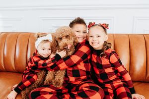 A group wearing matching red and black buffalo plaid outfits sits together on a brown leather couch.