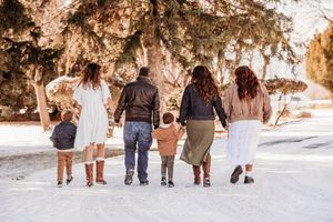 A group of people walking together in winter snow holding hands, photographed from behind at sunset.
