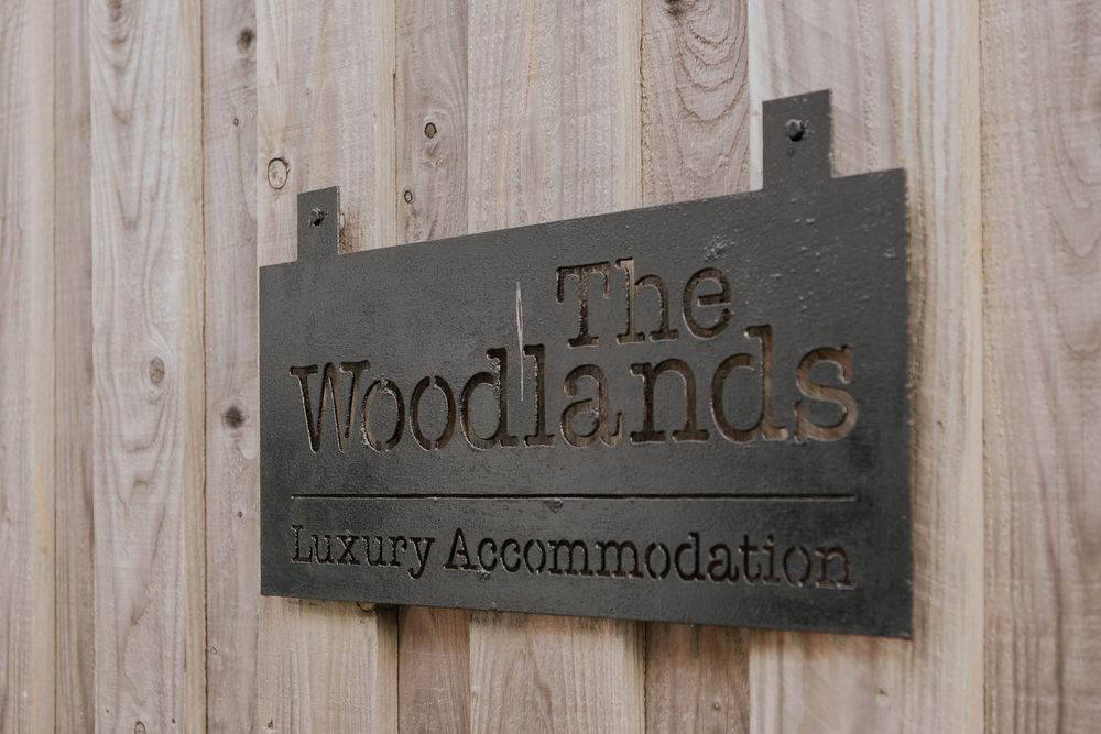 Rustic wooden sign reading The Woodlands Luxury Accommodation mounted on a timber wall.