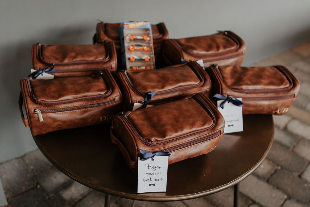 Brown leather toiletry bags arranged on a round table with gift tags and Hot Wheels toys.