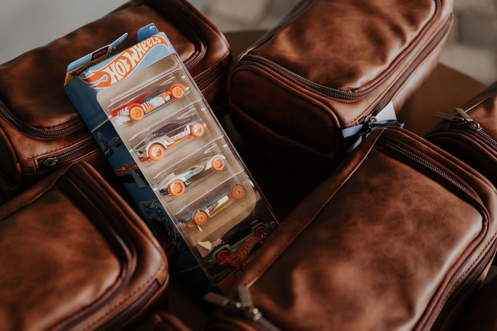 Hot Wheels toy car pack resting on brown leather toiletry bags as groomsmen gifts.