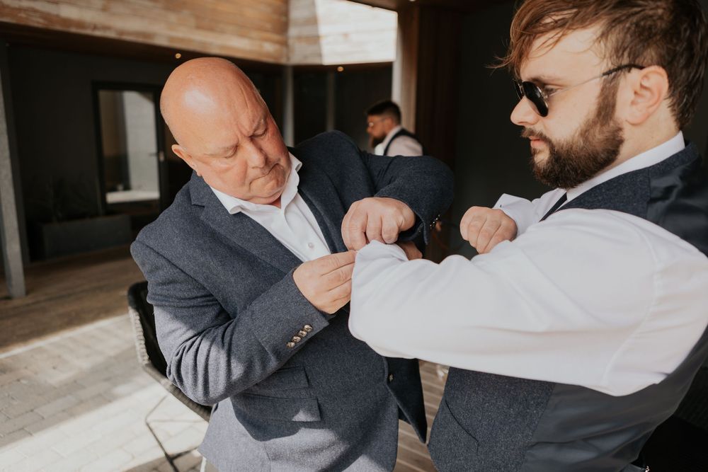 Two men in wedding attire adjusting suit jackets during groomsmen preparations before the ceremony.