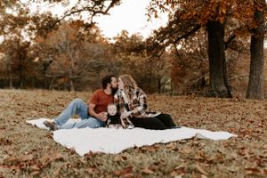 A couple lounges on a white blanket in an autumn field during a romantic outdoor photoshoot.
