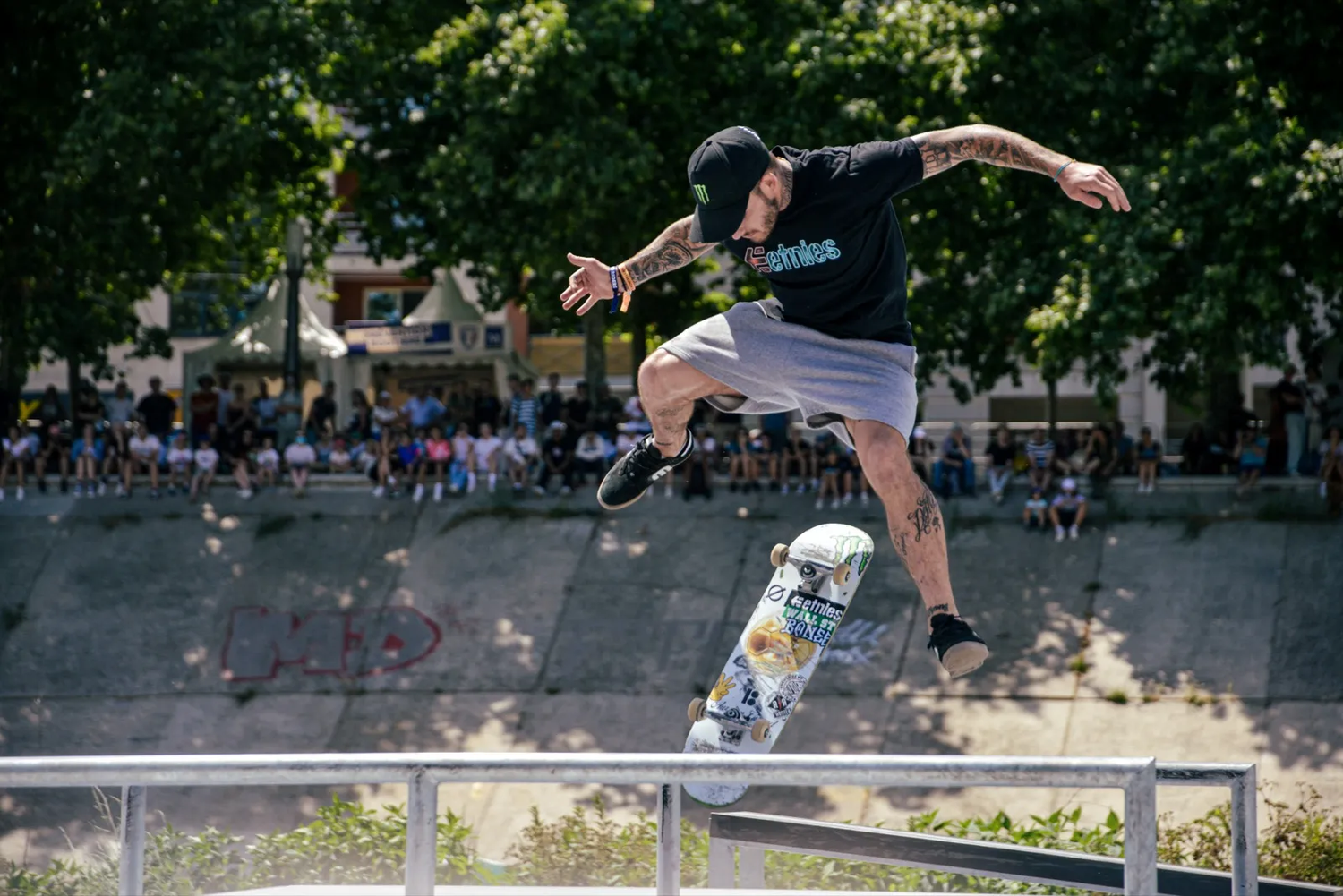 Skateur réalisant une figure au-dessus d’une barre de métal devant une foule en extérieur.