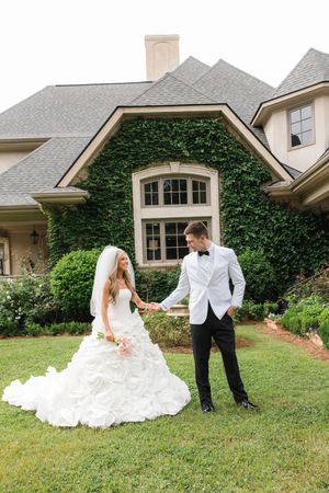 A bride and groom hold hands on a green lawn in front of an ivy-covered estate home on their wedding day.
