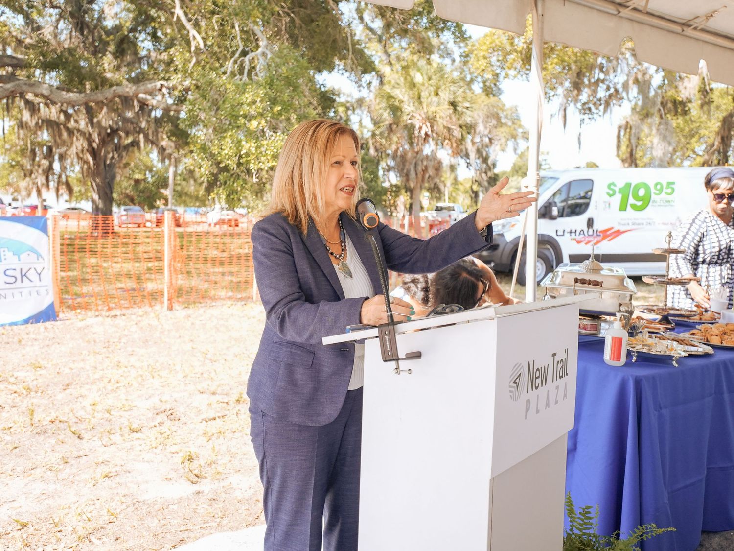 A speaker presents at an outdoor podium during a sunny daytime event.