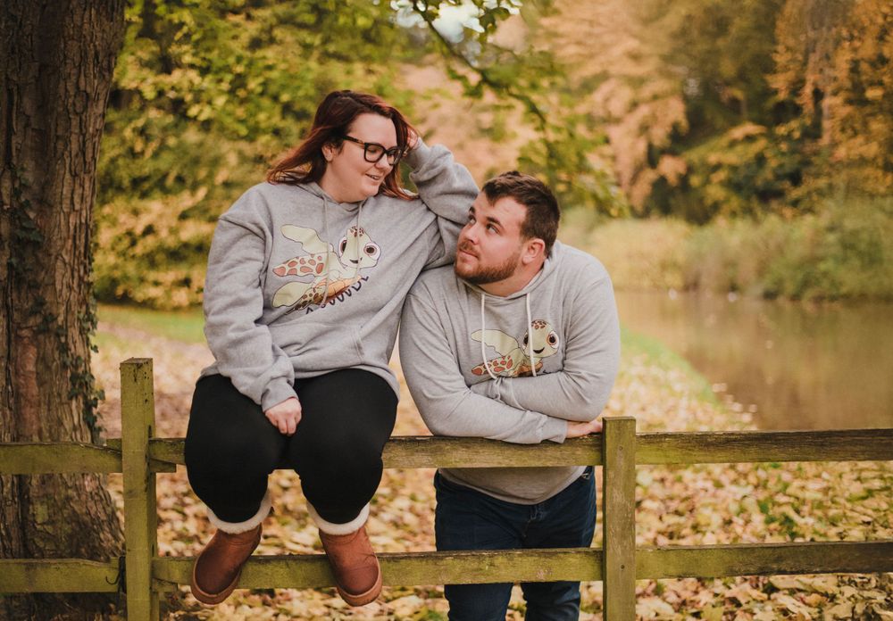 Two people sit together on a wooden fence sharing a tender moment in autumn scenery.