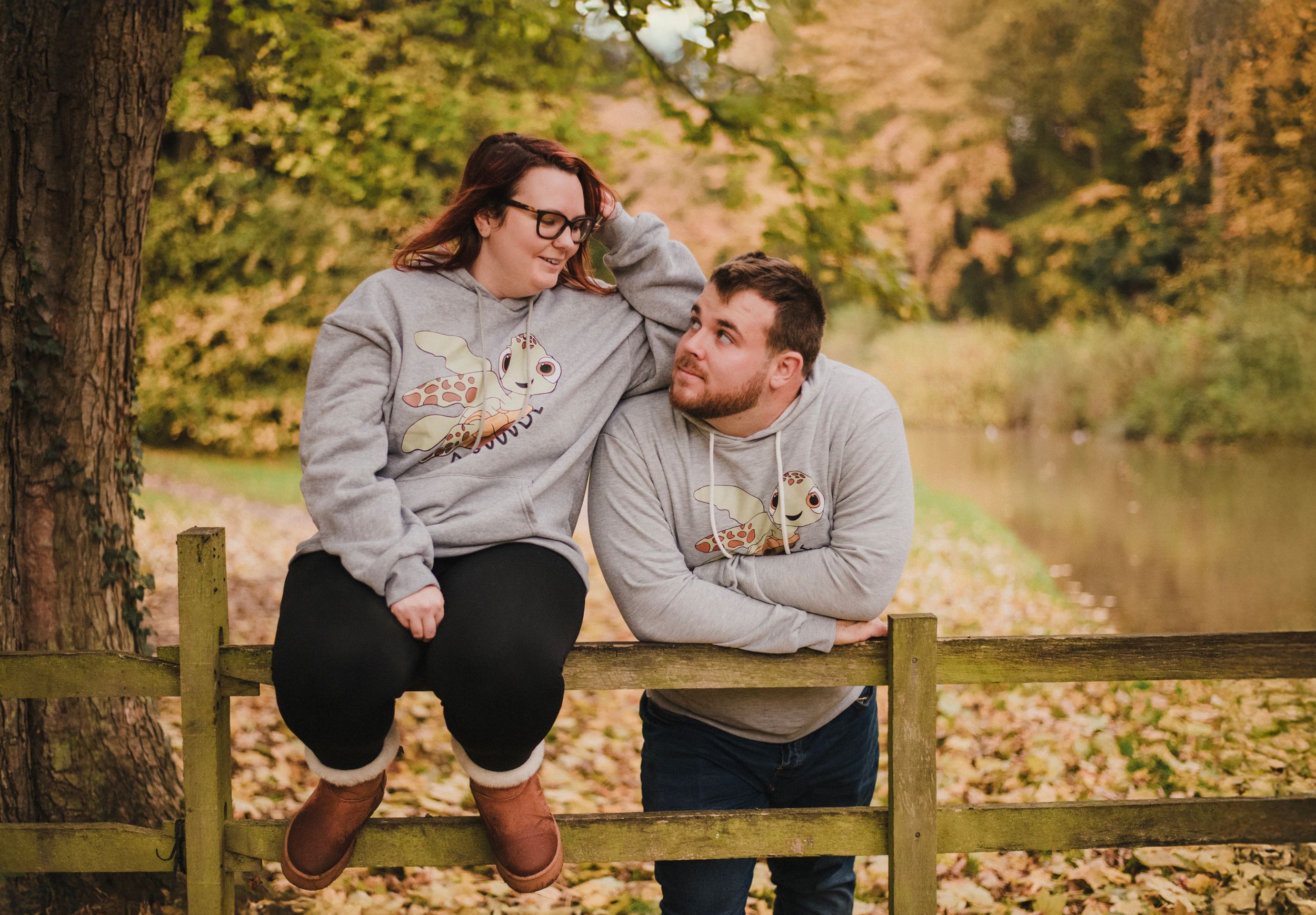 Two people sit together on a wooden fence sharing a tender moment in autumn scenery.