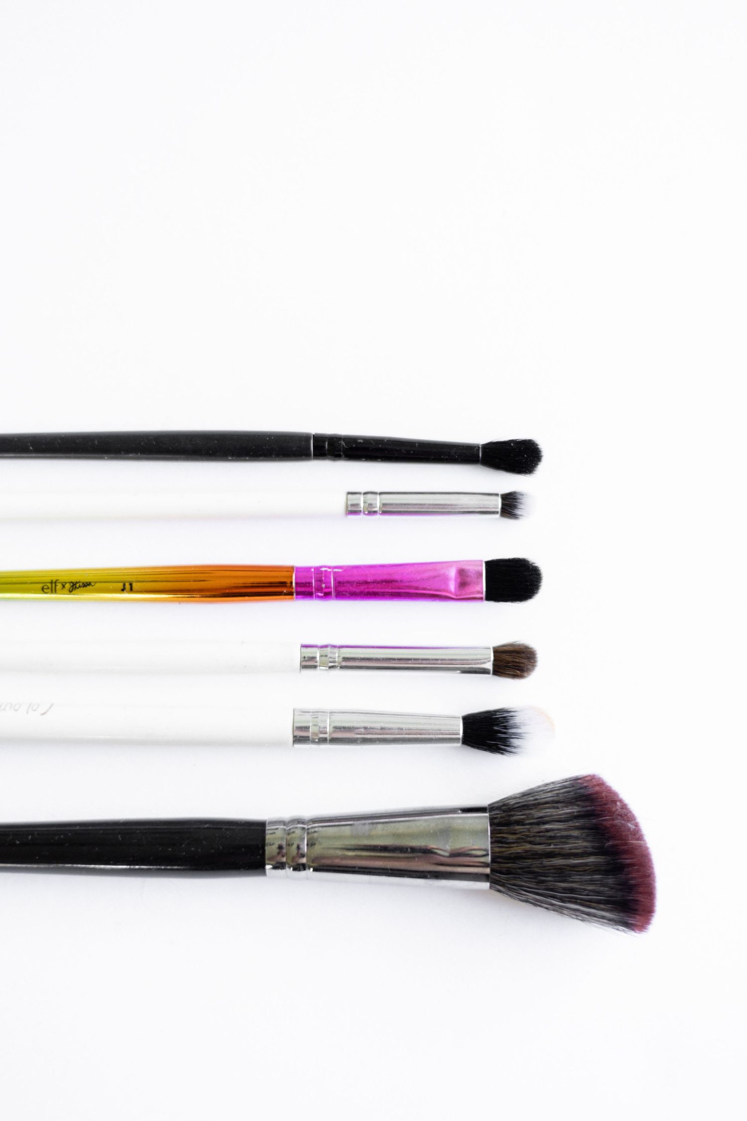 White background close up details of makeup artist brushes laid out.